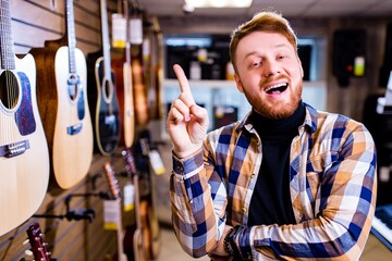 Irishman with red ginger hair and beatd is considering a guitars in a music store
