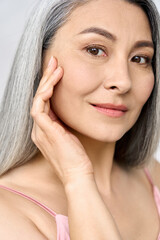 Senior older middle aged Asian woman's face with perfect skin. Older mature lady touching face. Advertising of dermatology cosmetology salon spa procedures skincare. Vertical portrait.