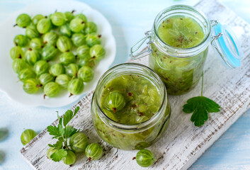 A small glass jar with homemade jam and the fresh gooseberry berries on a white background. Selective focus.