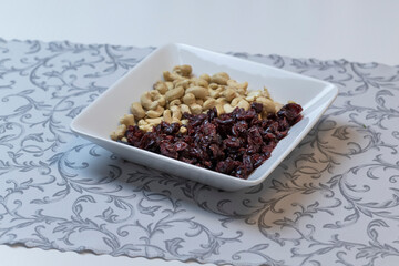 White bowl with cashews and cranberries set on table.