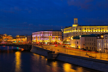 A bright blue evening in Moscow with a view of the river, Yakimanskaya embankment and old houses in the light of evening lamps.