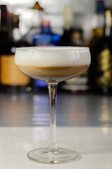 Alcoholic coffee cocktail with a nutty note and fluffy milk foam on the background of the bottles at the bar