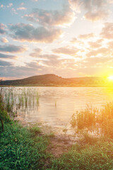 Bright summer sunrise over a lake with hills and clouds in the sky
