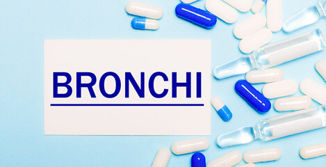 Pills, ampoules and a white card with the text BRONCHI on a light blue background. Medical concept