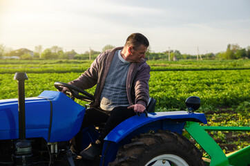 Fototapeta premium A farmer drives a tractor while harvesting potatoes. First potato harvest in early spring. Agro industry and agribusiness. Harvesting mechanization in developing countries. Farming and farmland.