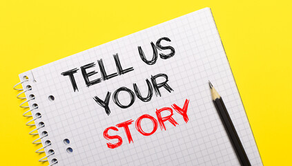 White notebook with inscription TELL US YOUR STORY written in black pencil on a bright yellow background.