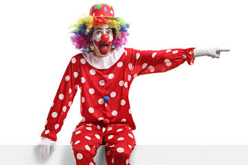 Funny clown sitting on a white panel and pointing to the side