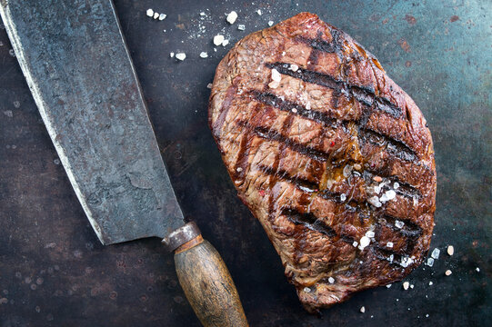 Barbecue dry aged entrecote double beef steak with salt and a kitchen cleaver served as top view on a rustic board