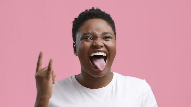 Funny African Woman Gesturing Rock Sign Showing Tongue, Pink Background