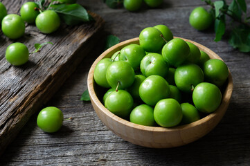 Fresh ripe organic green plums or greengage in bowl on wooden background, heap of summer fruits concept
