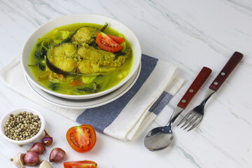 Pindang Ikan Patin or Catfish vegetables Soup , Indonesian food popular from Palembang. Served on ceramic bowl garnished with tomato slices. White marble background.
