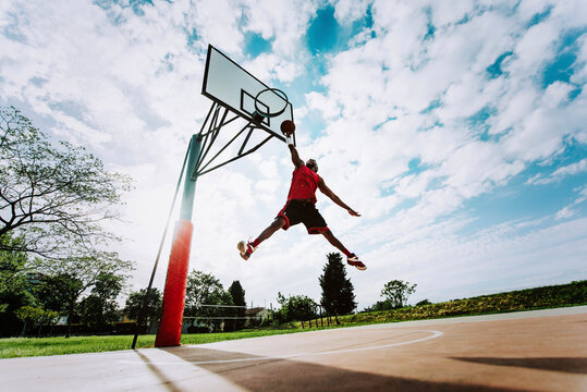 Street basketball player making a powerful slam dunk on the court - Athletic male training outdoor at sunset - Sport and competition concept