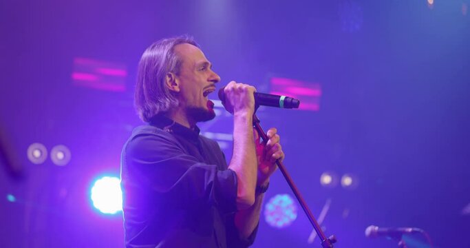 Expressive singer singing into microphone. Live music concert in front of bright colorful strobing lights on stage. Slow motion