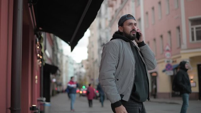 Young, modern handsome man talking on the phone on the street of a small town