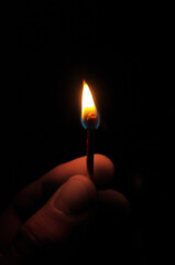 Light of fire from a match while being held by a hand with a black background and darkness around