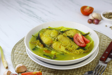 Pindang Ikan Patin or Catfish vegetables Soup , Indonesian food popular from Palembang. Served on ceramic bowl garnished with tomato slices. White marble background.