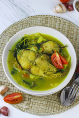 Pindang Ikan Patin or Catfish vegetables Soup , Indonesian food popular from Palembang. Served on ceramic bowl garnished with tomato slices. White marble background.