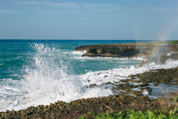the waves of the Caribbean sea crash against the rocks and the rainbow by the cliff