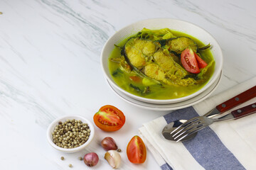 Pindang Ikan Patin or Catfish vegetables Soup , Indonesian food popular from Palembang. Served on ceramic bowl garnished with tomato slices. White marble background.