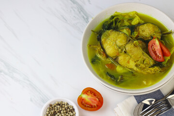 Pindang Ikan Patin or Catfish vegetables Soup , Indonesian food popular from Palembang. Served on ceramic bowl garnished with tomato slices. White marble background.