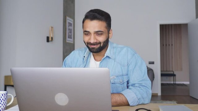 Young happy indian male teacher talking on webinar video training using pc laptop at modern home office. Hispanic businessman on interview, talking to team online. Remote distant online work concept.