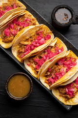 Pork tacos called cochinita pibil with purple onion on dark background. Mexican tacos