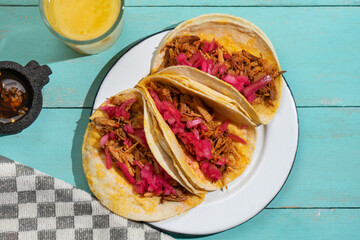Pork tacos called cochinita pibil with purple onion on turquoise background. Mexican tacos