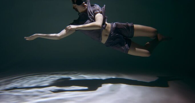 Having a dream sleeping. Young attractive woman in pyjamas, sleep mask sinking under water in swimming pool slow motion.