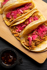 Pork tacos called cochinita pibil with purple onion on dark background. Mexican tacos