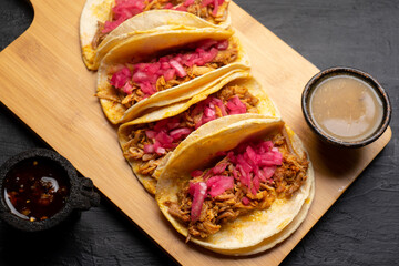 Pork tacos called cochinita pibil with purple onion on dark background. Mexican tacos