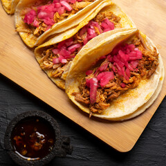 Pork tacos called cochinita pibil with purple onion on dark background. Mexican tacos