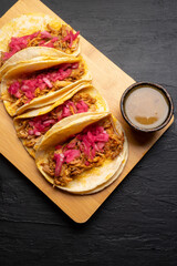 Pork tacos called cochinita pibil with purple onion on dark background. Mexican tacos