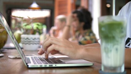Close up of female hands typing on a laptop and drinking matcha ice tea latte.Remote work concept. 