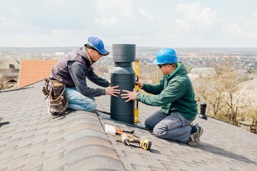workers on the roof installing tin cap on the iron chimney. roofing Construction and Building New iron House with Modular Chimney,