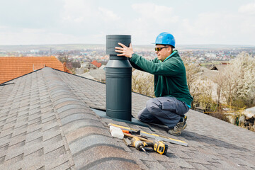 worker with blue helmet on the roof installing iron chimney. roofing Construction and Building New...