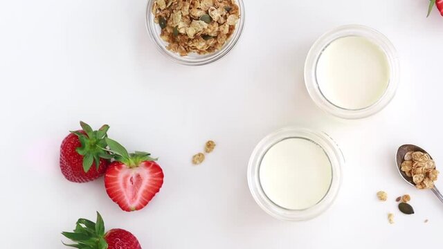 Greek yogurt in a glass jar with muesli and strawberries at the white table.