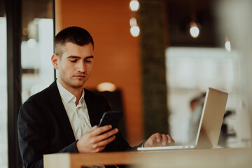 Happy business man sitting at cafeteria with laptop and smartphone.