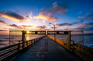 Ocean beach fishing pier in San Diego California during colorful sunset with a sun star and bird...