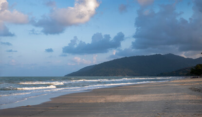 Calmful ocean beach sunset with mountain, bright blue sky and breezing waves in Kanom, nakhon si thammarat, Thailand