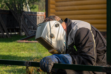 Close up of a young  man welder in  uniform, welding mask and welders leathers, weld  metal  with a...