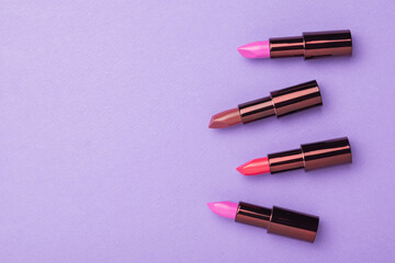 A banner with four tubes of lipstick on a purple background. Space for the text. Flat lay. - obrazy, fototapety, plakaty