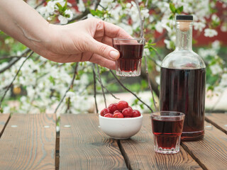 Hand with a glass of cherry alcoholic drink on the background of a flowering tree.