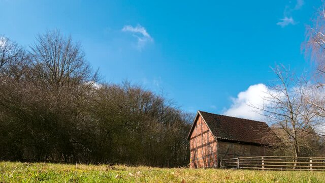 Time lapse of beautiful old timbered and red brick barn on a farm with huge green grass field near Hamburg in Kiekeberg, Germany.