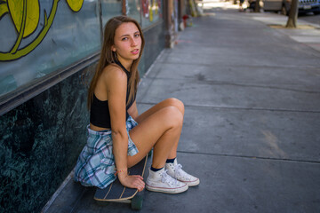 Naklejka premium Young Woman Seated With Skateboard on the Sidewalk in a Downtown Area