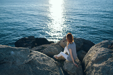 woman traveler sitting on stones near the sea landscape beach sunset clear water