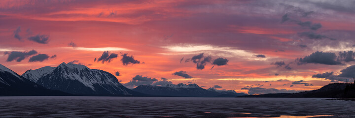 Stunning sunset over snow capped mountain peaks in northern Canada during spring time with purple, peach and pink colors in natural, wild setting. Taken in Warm Bay, Atlin, British Columbia, Canada. 