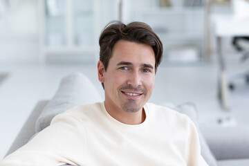 Close-up portrait of a handsome man has an attractive appearance, sits on a sofa against a cozy interior. Student posing