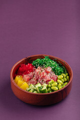 Hawaiian tuna poke bowl with vegetables on purple background