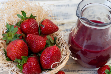 Strawberry in basket and on table on wooden background, strawberry juice in jug