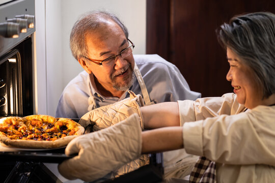 Asian Senior Woman Enjoy Cooking, Baking Pizza By Using Oven At Home.